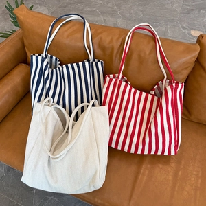 Three oversized striped canvas tote bags in navy, red, and beige on a brown leather sofa