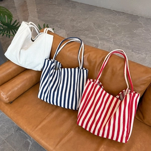 Three oversized canvas tote bags in white, blue and red stripes on a leather sofa