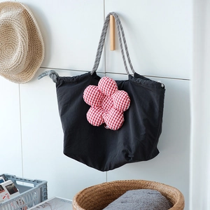 Detail of a black drawstring lunch bag with a red plaid plush flower and woven handles