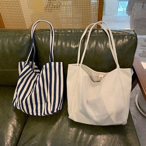 Detail of striped and beige canvas tote bags resting on a green leather sofa