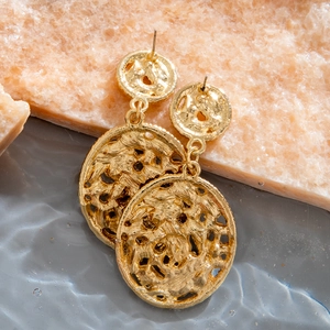 Detail of gold dangle earrings with irregular lava texture on textured stone background