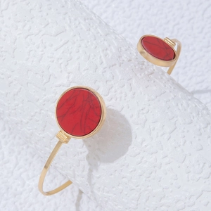 Macro view of gold open bangle featuring round red faux stone inlays on both ends