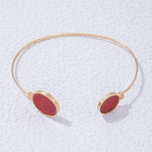 Detail of a gold open bangle set with two oval red gemstones featuring natural black textures