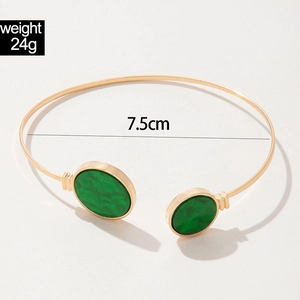 Detail view of gold cuff bracelet with green gemstones showing 7.5cm diameter and 24g weight