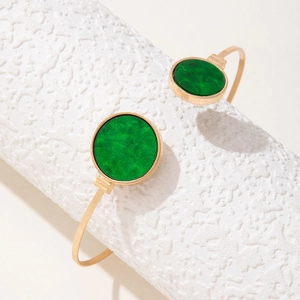Detailed shot of a gold-plated open cuff bracelet with two emerald green resin stones