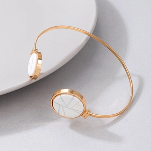 Detail of a gold open bangle with a white marble disc on a minimalist background