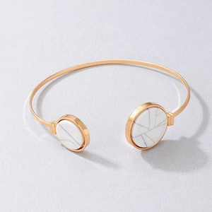 Detail of gold open bangle featuring circular white marble stone ends on textured background