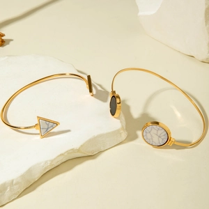 Detail of two gold open bangles with geometric marble insets on stone display