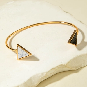 Detailed shot of an open gold bangle with marble-textured triangle stone ends on white stone