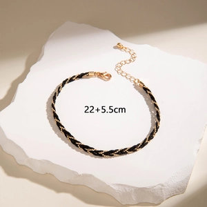 Detalle de tobillera trenzada negra con cuentas doradas y cadena de extensión de 22+5,5 cm
