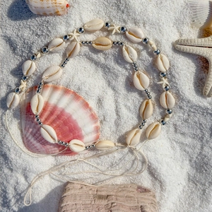Detail of shell necklace with metal starfish charms on white beach sand