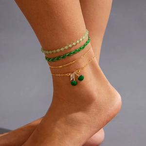 Close-up of layered beaded anklets featuring a gold cherry pendant with sparkling crystals