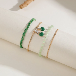 Close-up of four-piece bracelet set with green woven rope and gold cherry pendant