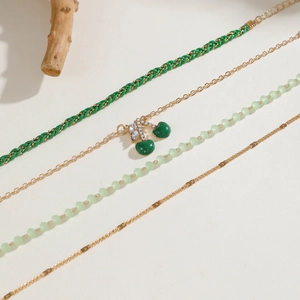 Detail of multi-layer jewelry set with green cherry pendants and mixed beaded gold chains
