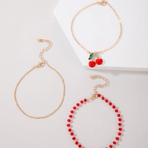 Close-up of three-piece beaded anklet set with red cherry charms and crystal details