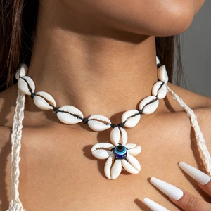Detail of shell necklace featuring a floral pendant with a blue evil eye bead on model