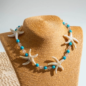 Detail of seashell necklace featuring white starfish charms and turquoise beads on grass stand