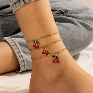 Close-up of triple layered gold anklet featuring red rhinestone cherry charms on the ankle