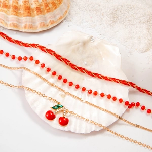 Detailed view of red bead anklet set with rhinestone cherry pendants on white seashell sand