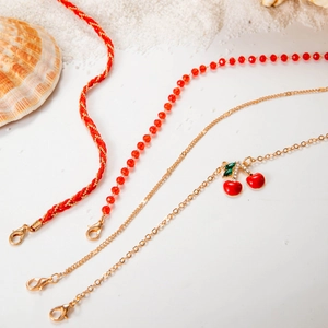 Detail of red beaded anklet set with crystal cherry pendant on sandy beach background