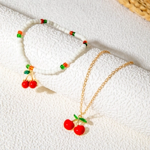 Detailed view of red cherry pendant beaded bracelet and gold chain necklace set