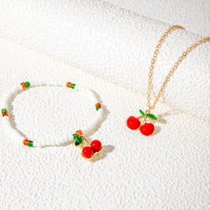 Detail shot of a beaded cherry bracelet and gold-tone necklace with red cherry pendants