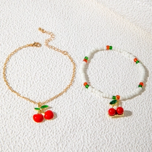 Detail of red cherry charms on gold chain and beaded anklets set for women