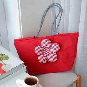 Close-up of red insulated lunch bag with a plaid floral motif and woven rope handles