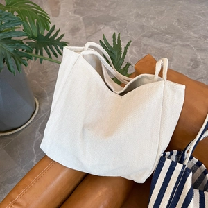 Close-up of white herringbone canvas tote bag on brown leather chair with green plant