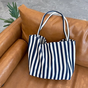 Detail of blue and white striped canvas tote bag on a brown leather sofa in home setting