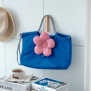 Blue drawstring lunch bag with red checkered flower detail and woven rope handles