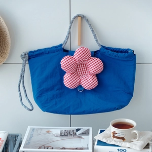 Detail of navy tote bag featuring a red checkered flower and braided rope handles