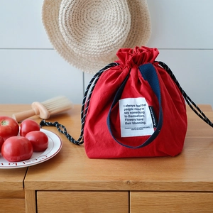 Detalle de bolsa de almuerzo térmica roja con cordón y asas tejidas en color azul