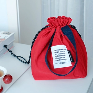 Detalle de bolsa de almuerzo roja y azul con cordón y etiqueta ArtisticSoul en mesa