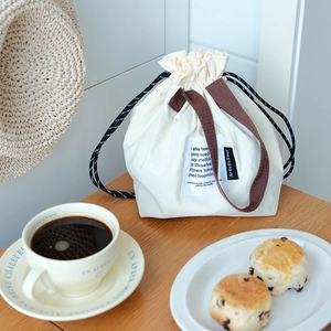 Detalle de bolsa de lona para almuerzo con cordón y asas marrones en mesa madera