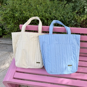 Dettaglio di borse tote in nylon trapuntato beige e blu con tasche frontali e logo in metallo