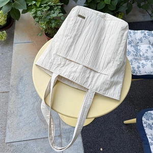 Dettaglio della borsa a tracolla plissettata con etichetta 'handmade' su tessuto crema