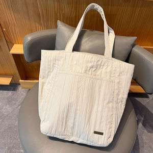 Dettaglio della trama plissettata della borsa beige e logo in metallo su nylon