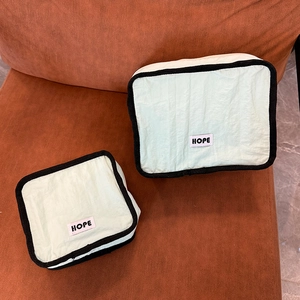 Detail of mint green makeup bags with HOPE label on orange textured background