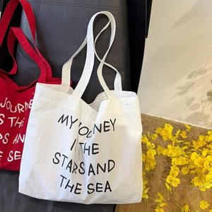 Detailed texture of white and red pleated nylon tote bags with printed slogan on sofa