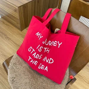 Detail of red canvas tote bag featuring white My Journey Is The Stars And The Sea lettering