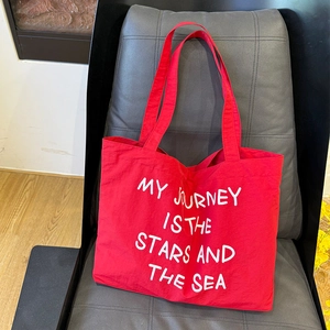 Detail of red canvas tote bag with 'MY JOURNEY' text and sturdy woven handles