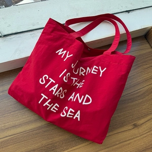Macro shot of red nylon tote bag with My Journey text on textured wood surface