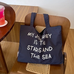 Detail of navy canvas tote bag with white inspirational text on a wooden chair