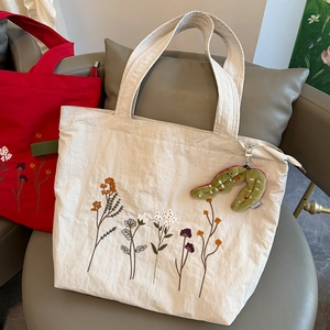 Close-up of floral embroidery on canvas tote bags with decorative plush pod charm