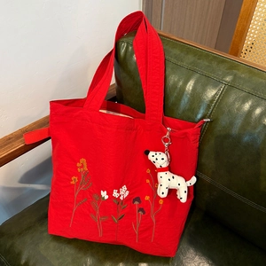 Detail of red nylon tote bag with floral embroidery and spotted dog plush charm