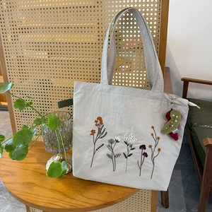 Detail of floral embroidery on beige canvas tote bag with colorful plush charm accessory