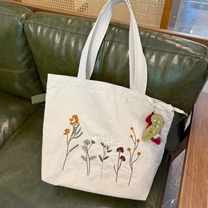 Detail of floral embroidery on beige nylon tote bag with cute plush pendant