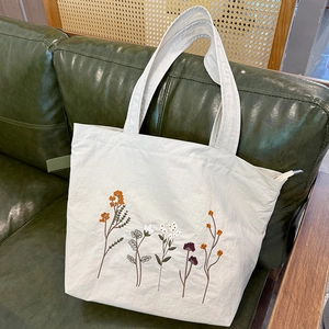 Close-up of vintage floral embroidery and zipper closure on a white nylon tote bag