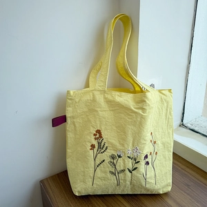 Close-up of colorful floral embroidery on a light yellow nylon tote bag with logo tag